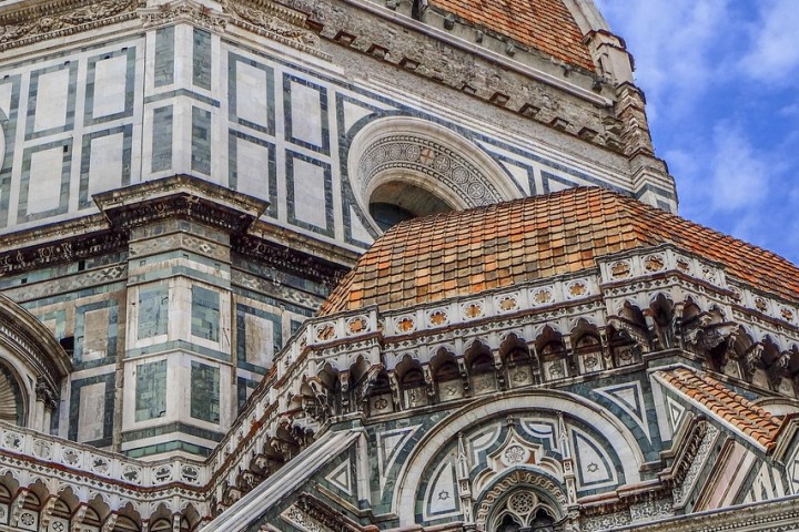 Close-up of Florence Cathedral facade and dome with tiled roof against a blue sky.