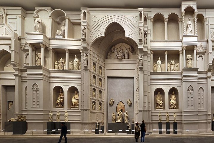 Intricate stone wall with arches, statues, and people observing indoors.
