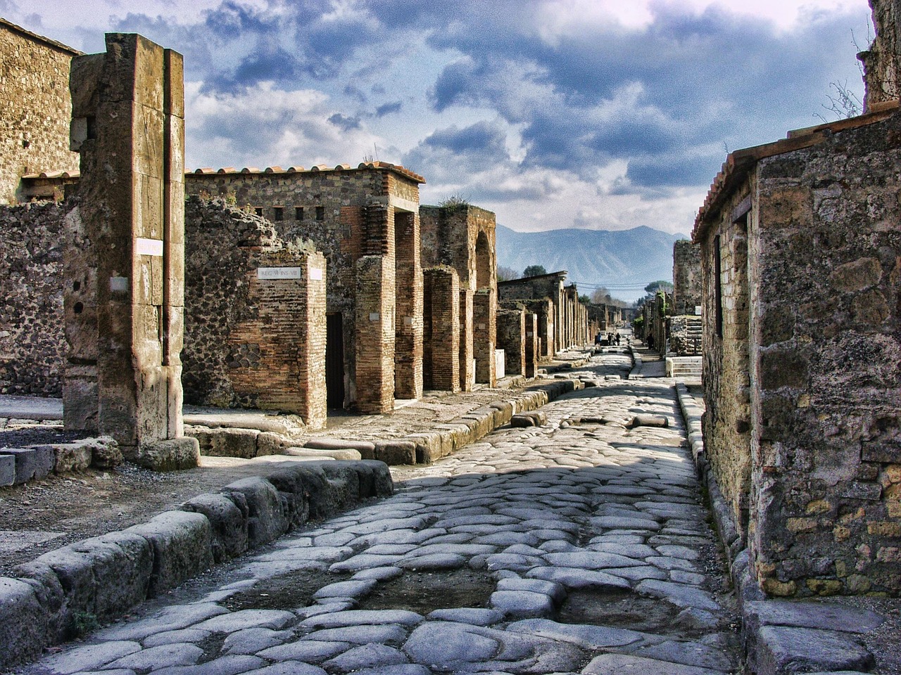 Ancient stone street in Pompeii with ruins and cloudy sky in background.