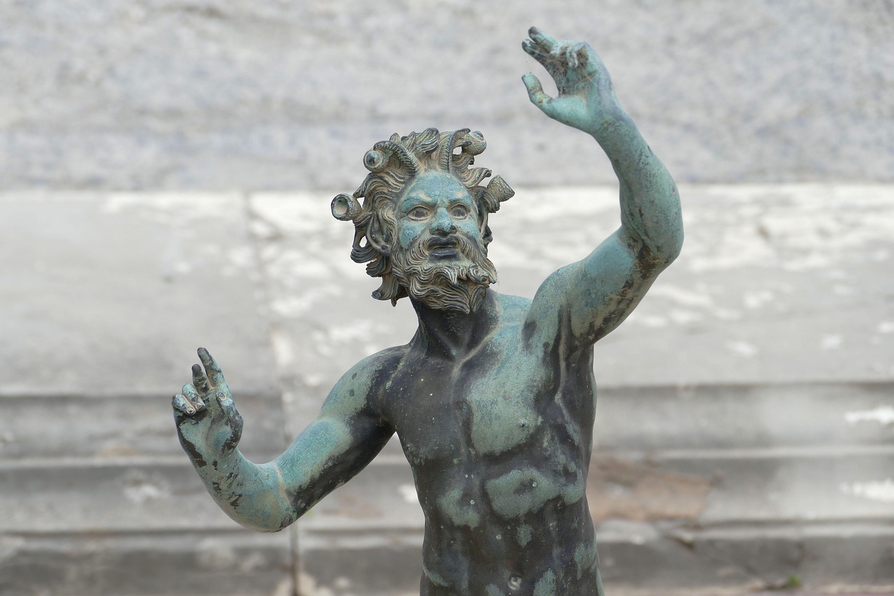Bronze statue of a mythological figure with wild hair and beard gesturing upward with both hands.