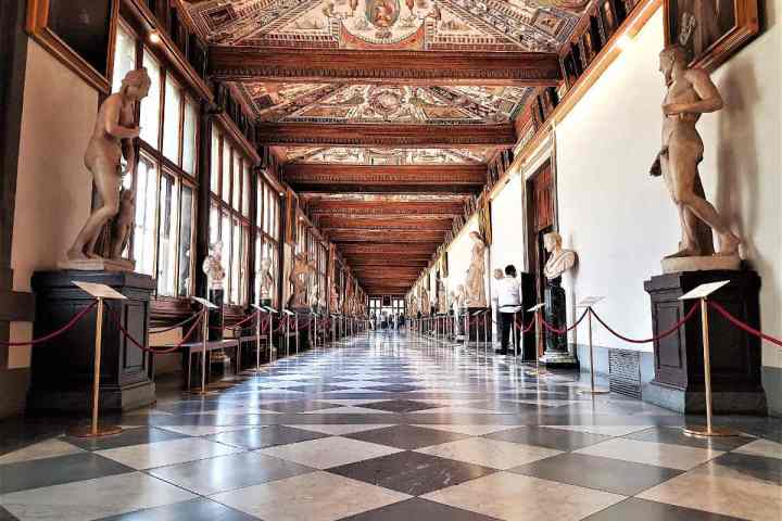 Ornate museum hallway with sculptures and paintings on either side, featuring a decorative ceiling.