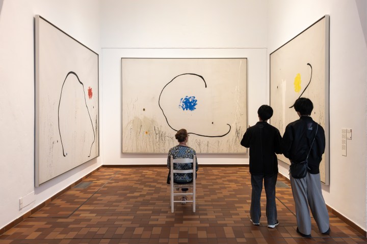 People viewing large abstract paintings in an art gallery.