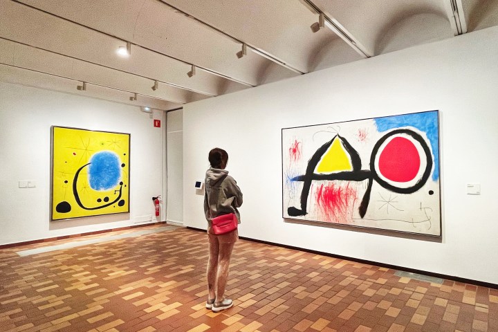 Person viewing abstract art in a gallery with geometric shapes and bright colors on two paintings.