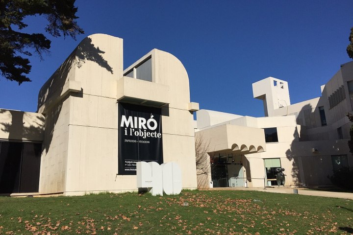 Modern white building with curved facades and a banner titled 'Miró i l'objecte' against a clear blue sky.