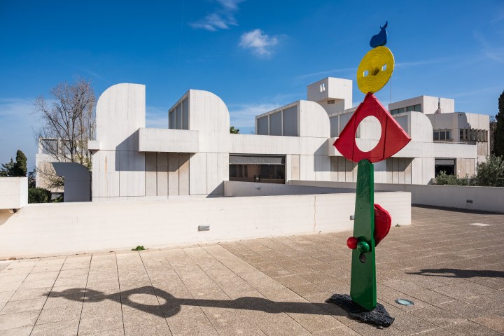 Modern sculpture in front of white geometric building under blue sky.