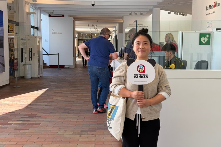 Woman holding a sign standing in a lobby area with people in the background.