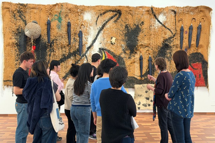 Group of people observing a large abstract textile artwork on a wall.