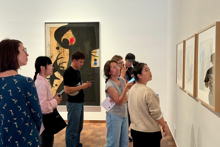 People viewing art in a gallery, some using smartphones and holding guides.