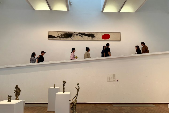 People walking up a modern art gallery ramp with sculptures and abstract painting.