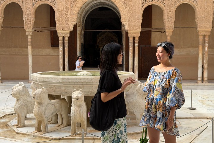 Two women talking by a stone fountain with lion statues.