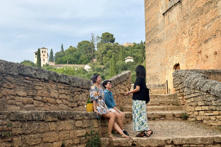 Three people sitting and talking on stone steps by an old building.