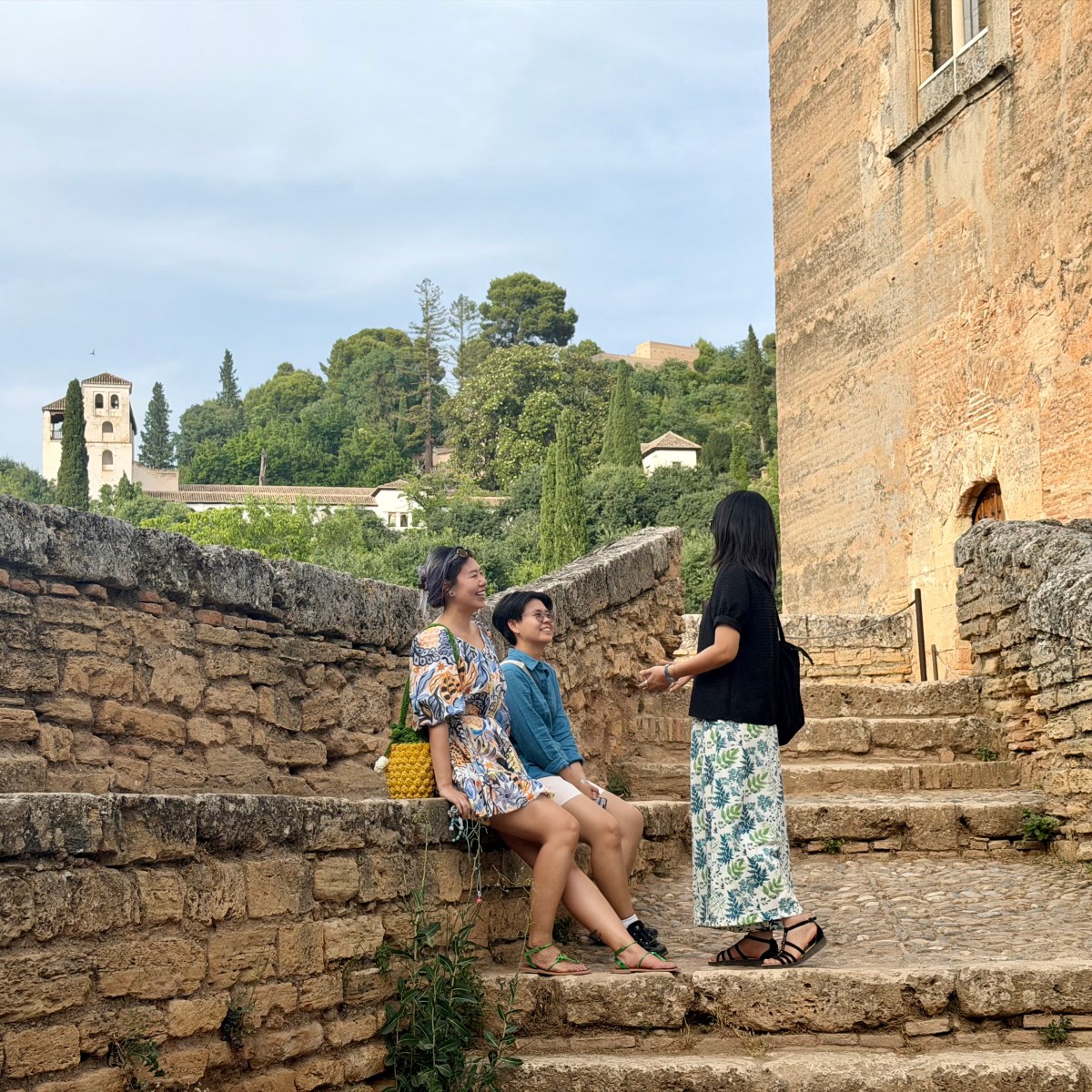Three people sitting and talking on stone steps by an old building.