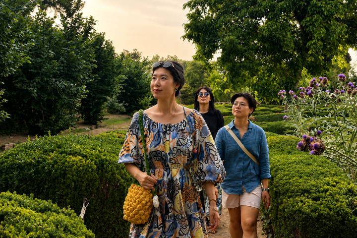 Three people walking through a garden with hedges and trees.
