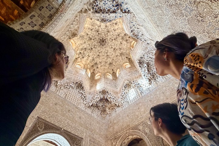 Three people looking up at intricate, decorative ceiling in a historic building.