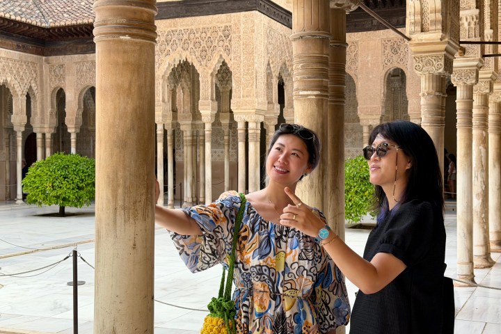 Two women admire the architecture in a historical courtyard with ornate columns.