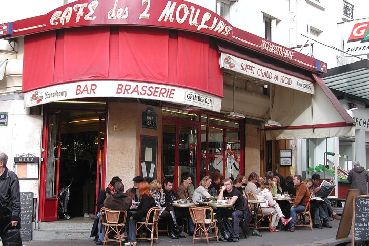 People sitting outside a café under a red awning on a city street.