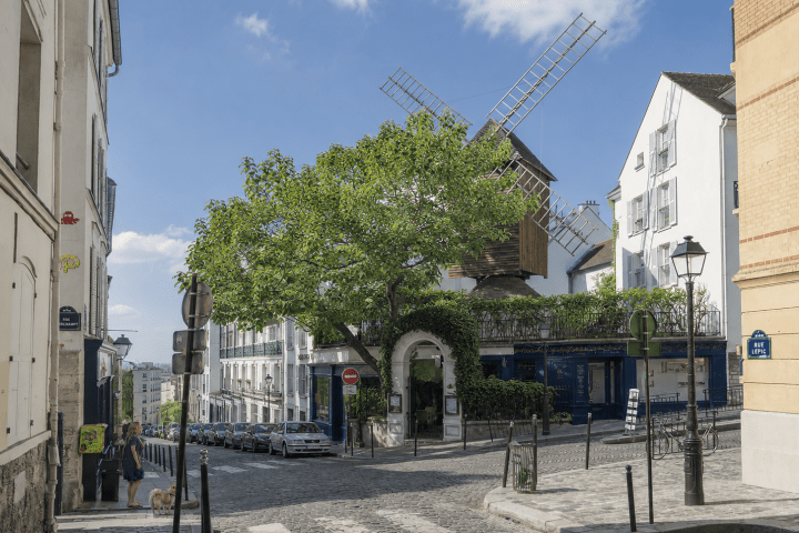 Street with windmill, tree, and buildings under blue sky.
