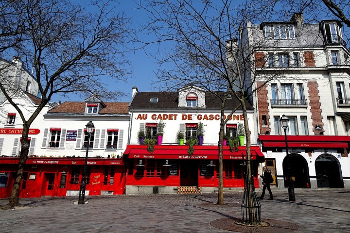 Outdoor view of red cafe buildings with trees and cobblestone street.