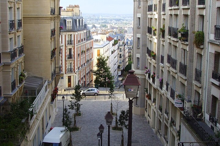 Steep cobblestone street with stairs between tall buildings in a cityscape view.