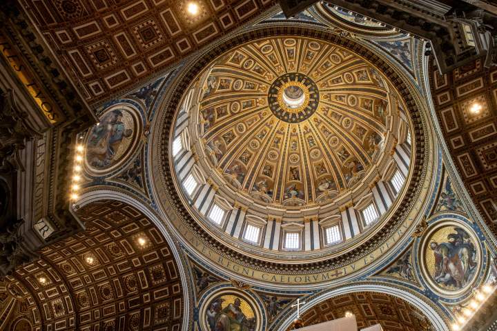 Intricate dome interior with ornate patterns and paintings in a cathedral.