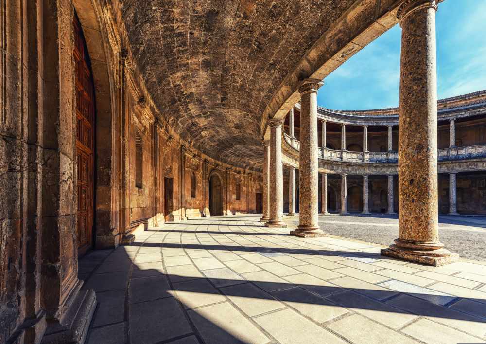 Curved stone colonnade with shadow patterns, sunny sky.