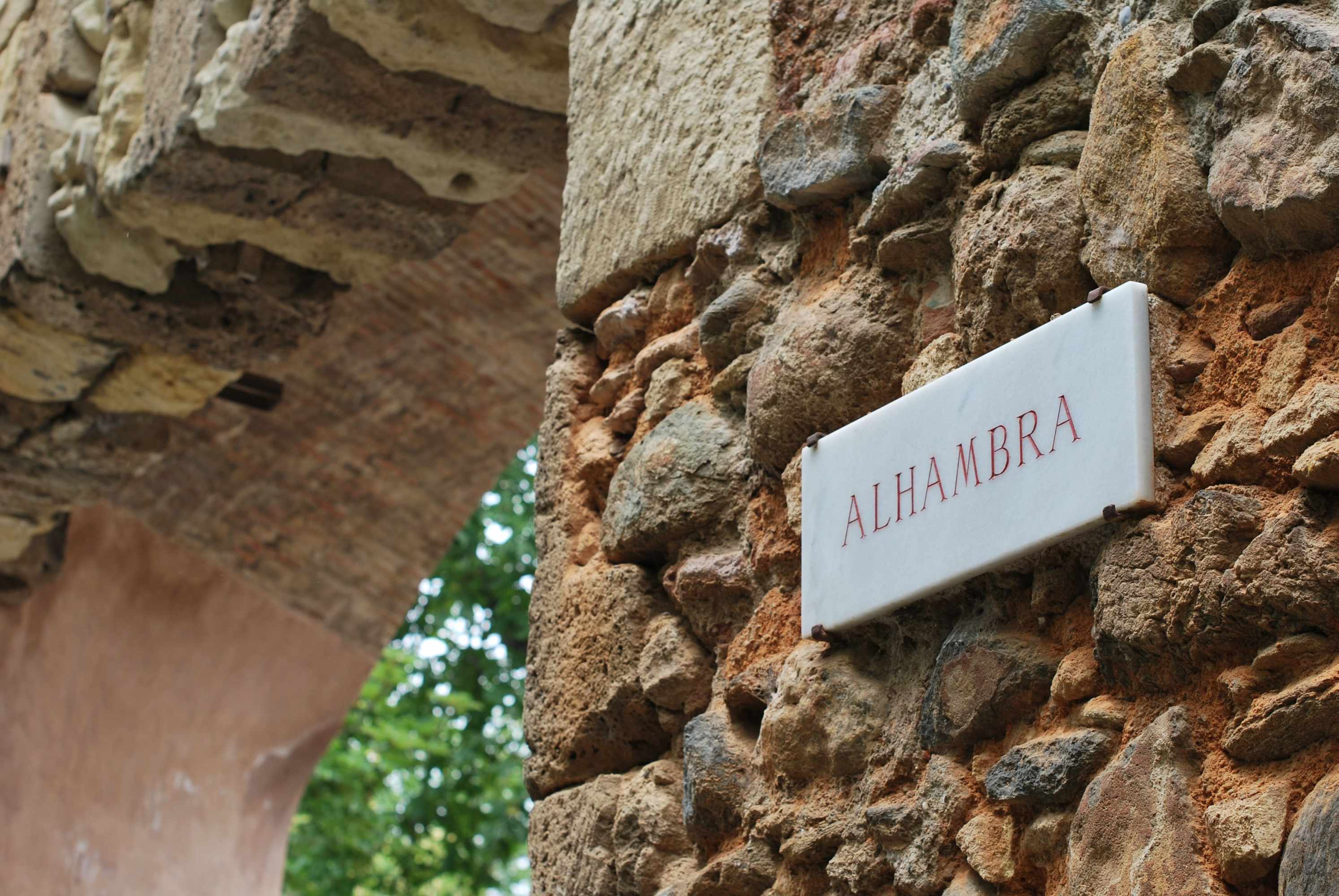 Stone wall with 'ALHAMBRA' sign near an archway.